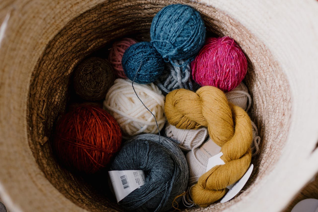Top view of various colorful yarn balls in a woven basket, perfect for knitting and crochet enthusiasts.
