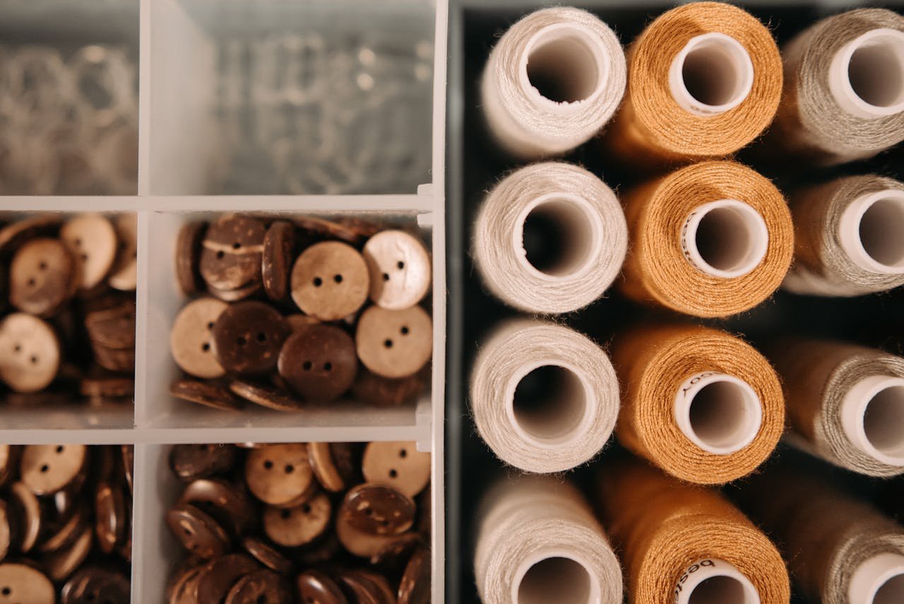 Close-up of spools of thread and wooden buttons in a container, arranged neatly.